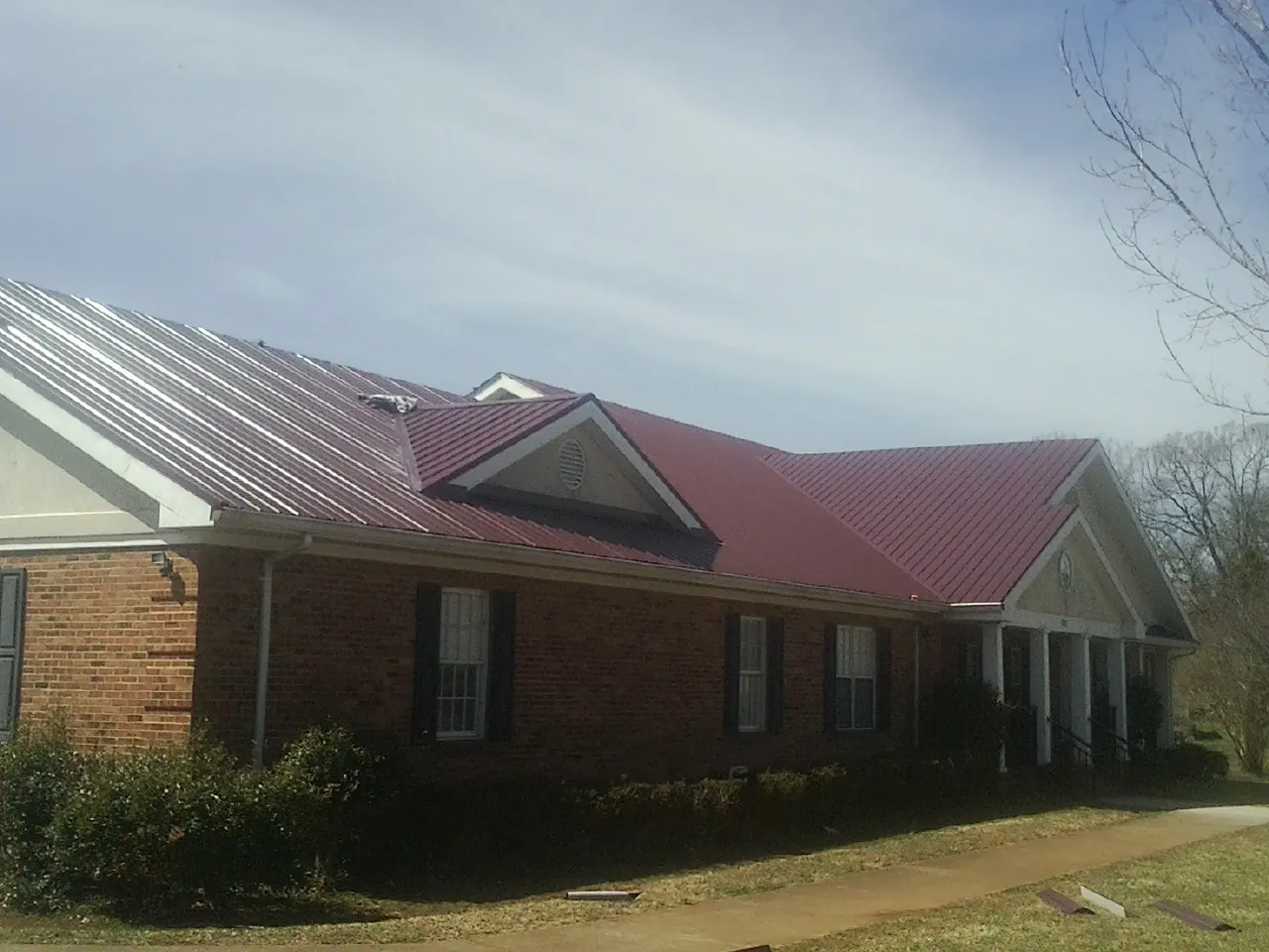 Red metal roof with gabled entries on a long brick building, from a Hail Damage Roof Repair job in Penrose