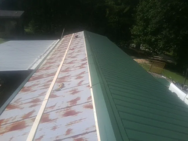 Old rusted panels beside newly installed green metal roofing — Wind Damage Roof Repair by Roofing Brothers in Penrose