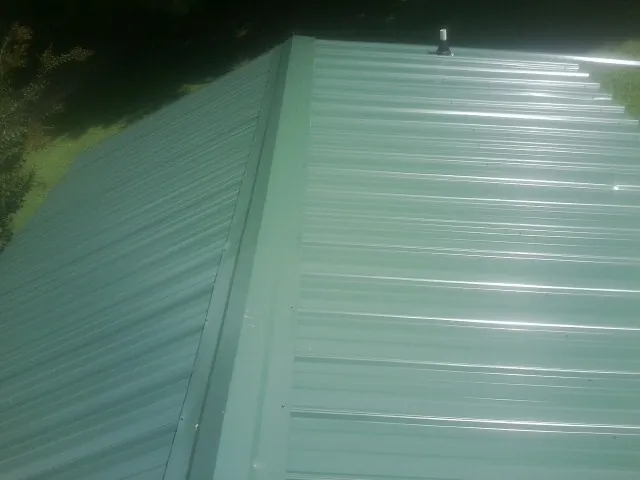 New green metal panels meeting at the ridge of a roof — Flat Roof Repair work by our crew in Penrose