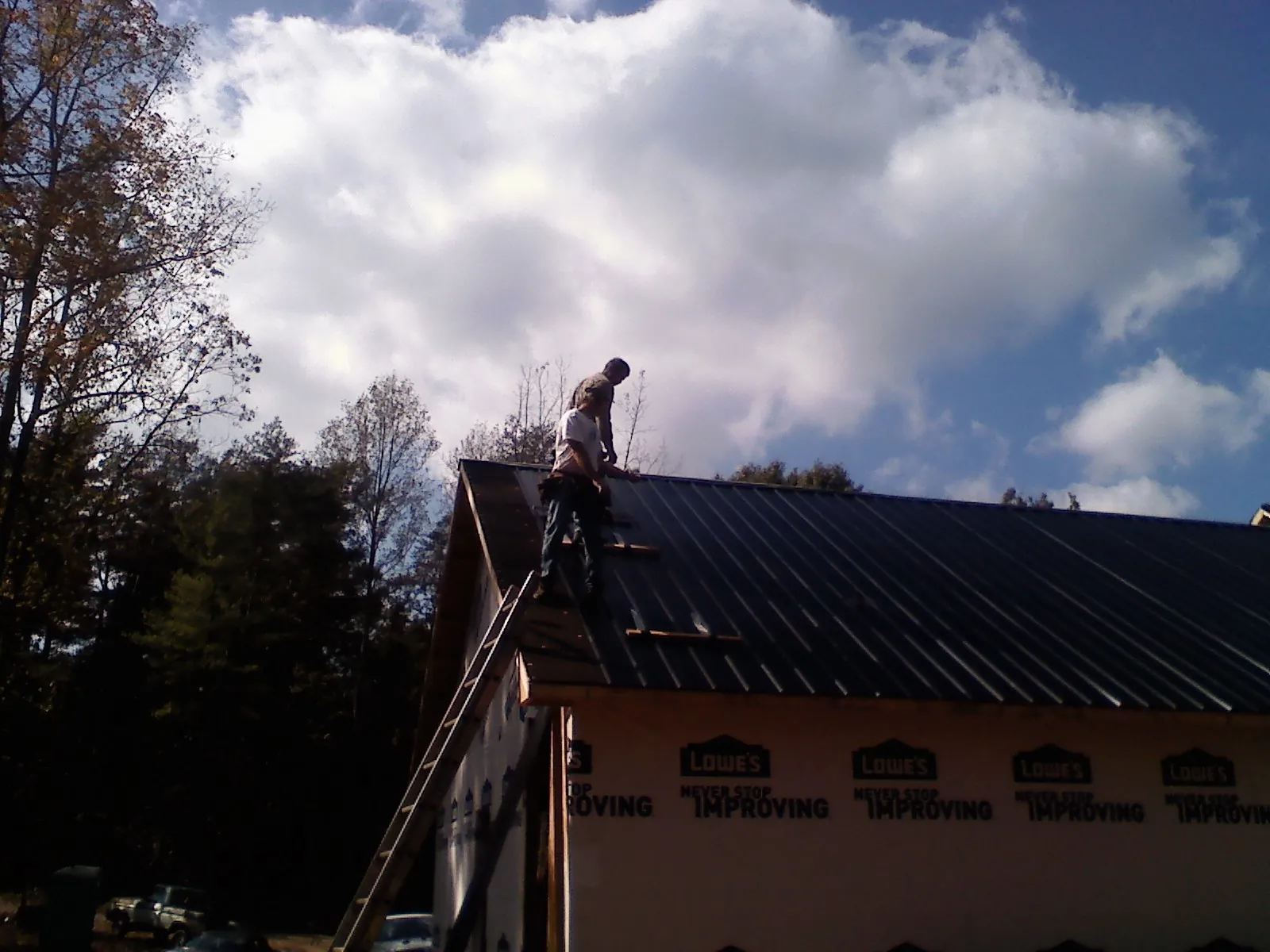 Roofer fastening dark metal panels high against a cloudy sky, from a Roof Inspection job in Penrose