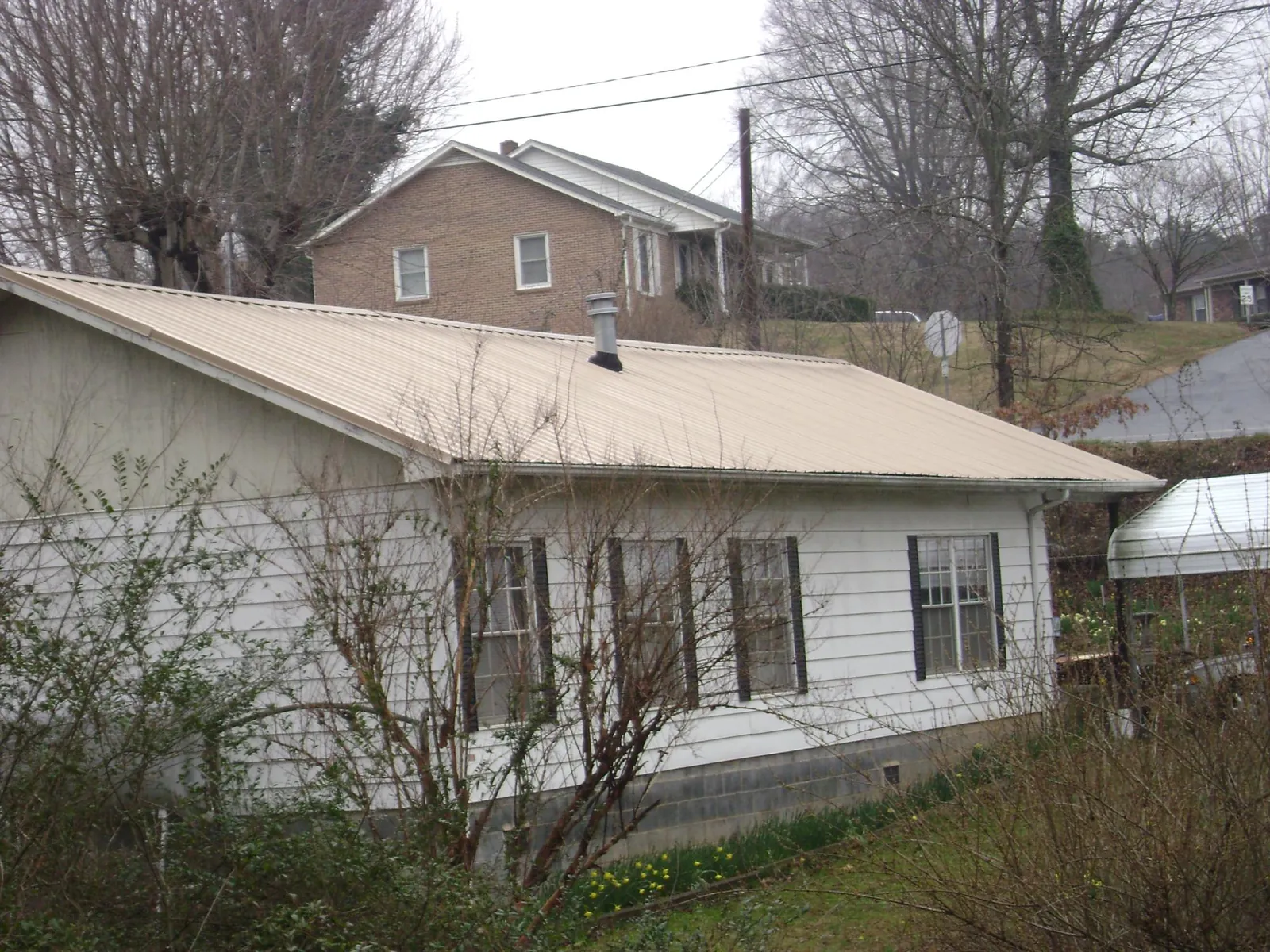 Tan metal roof on a white sided house set into a hillside — Commercial Roofing by Roofing Brothers in Penrose