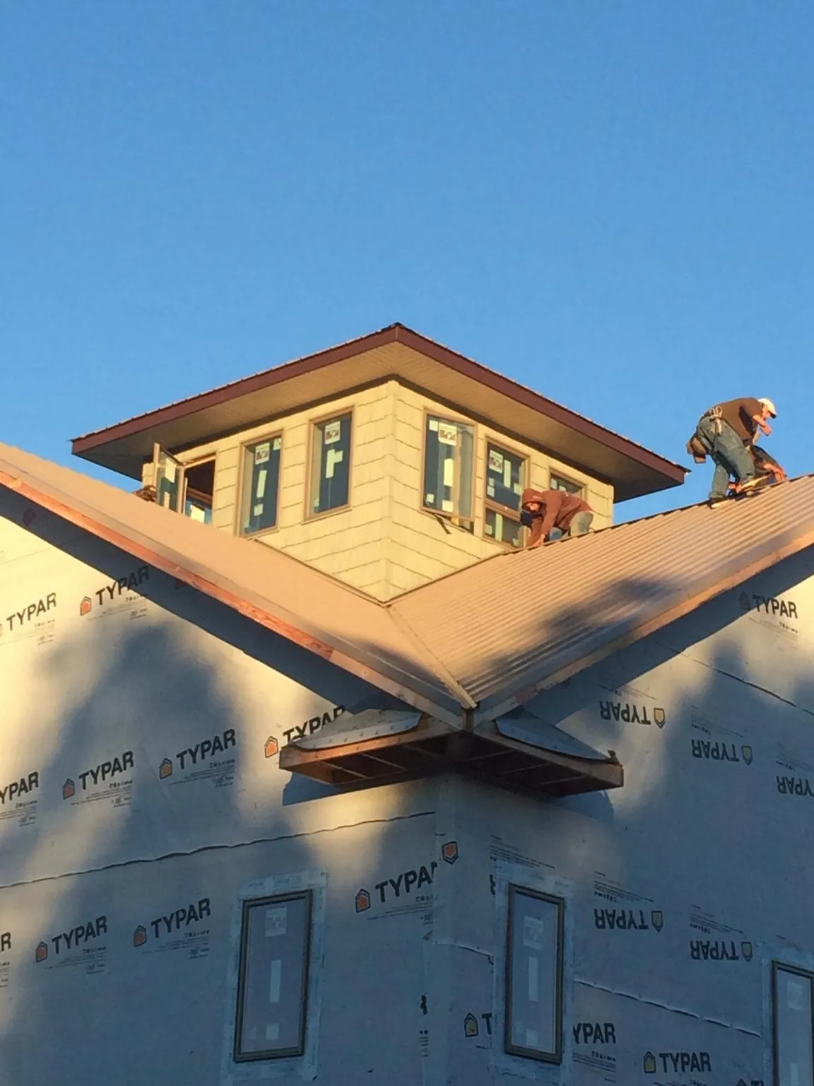 Roofers working around a rooftop cupola on a new metal roof at sunset — Roof Waterproofing in Penrose by Roofing Brothers